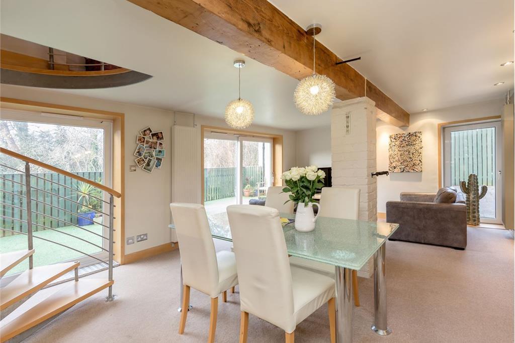 A very spacious dining and living area with white walls, very light brow carpet, and white furnishings.